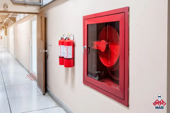 Imagen de gabinete metálico rojo de diseño robusto empotrado en una pared, protegiendo mangueras y su lado extintores para seguridad industrial
